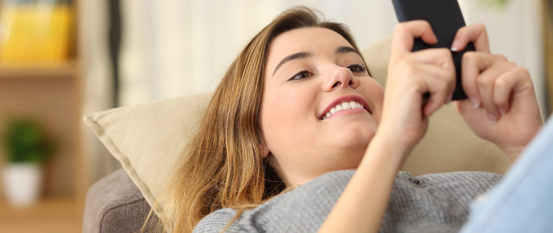 Kvinde ligger i sofaen og kigger glad på sin mobiltelefon